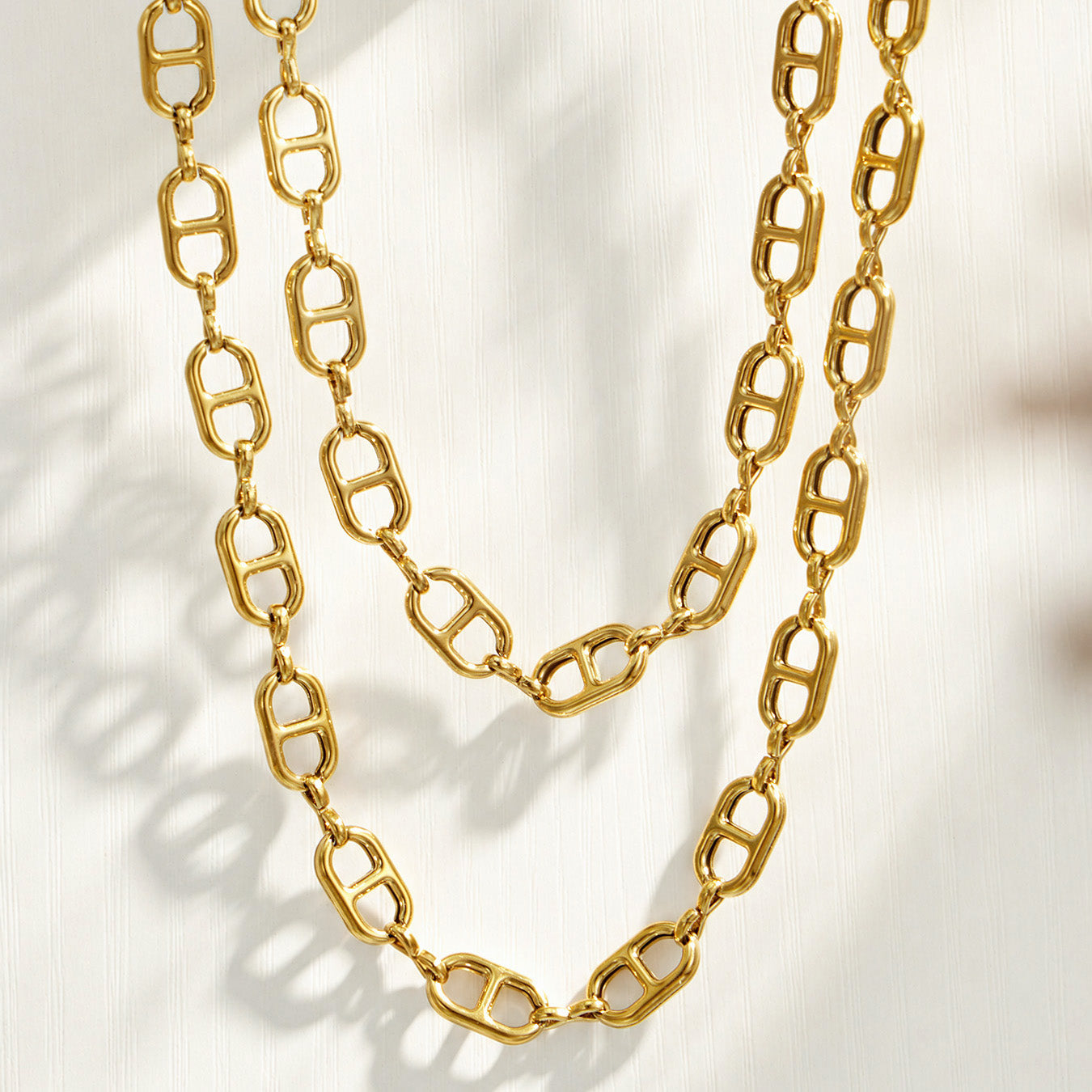 Layered gold mariner chain link necklaces displayed on a light textured surface
