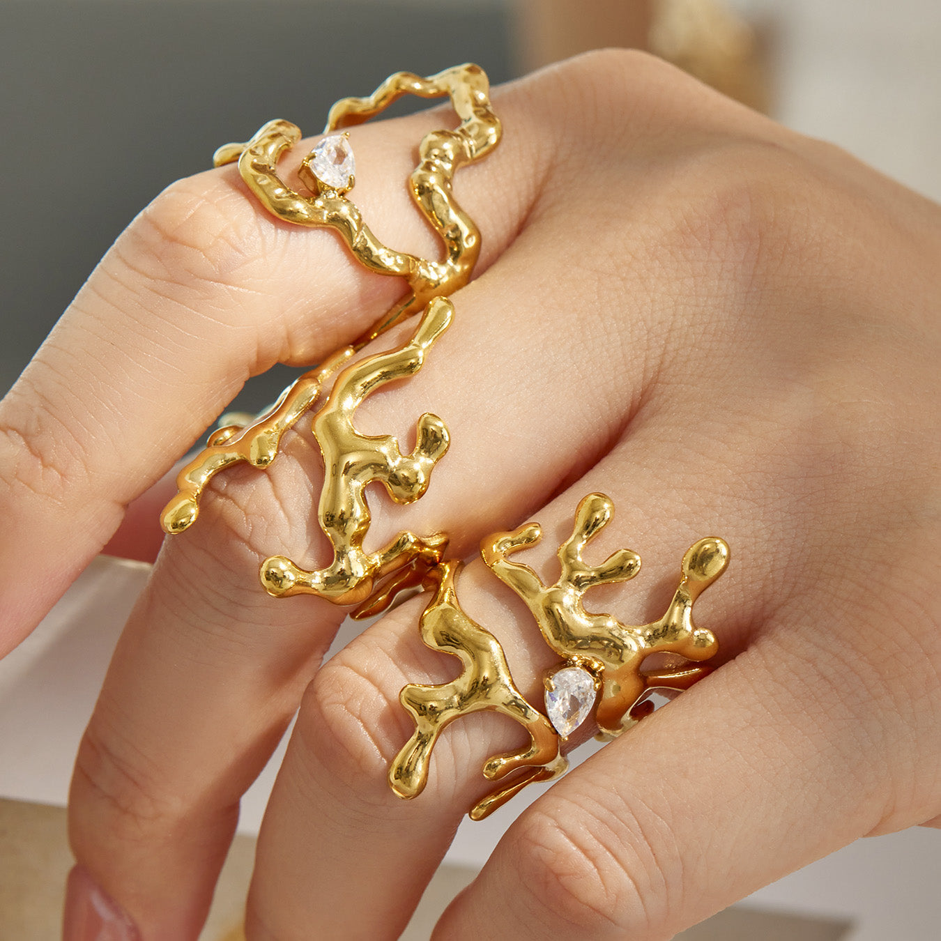 Model wearing gold molten-style 316L stainless steel statement rings with sculptural shapes