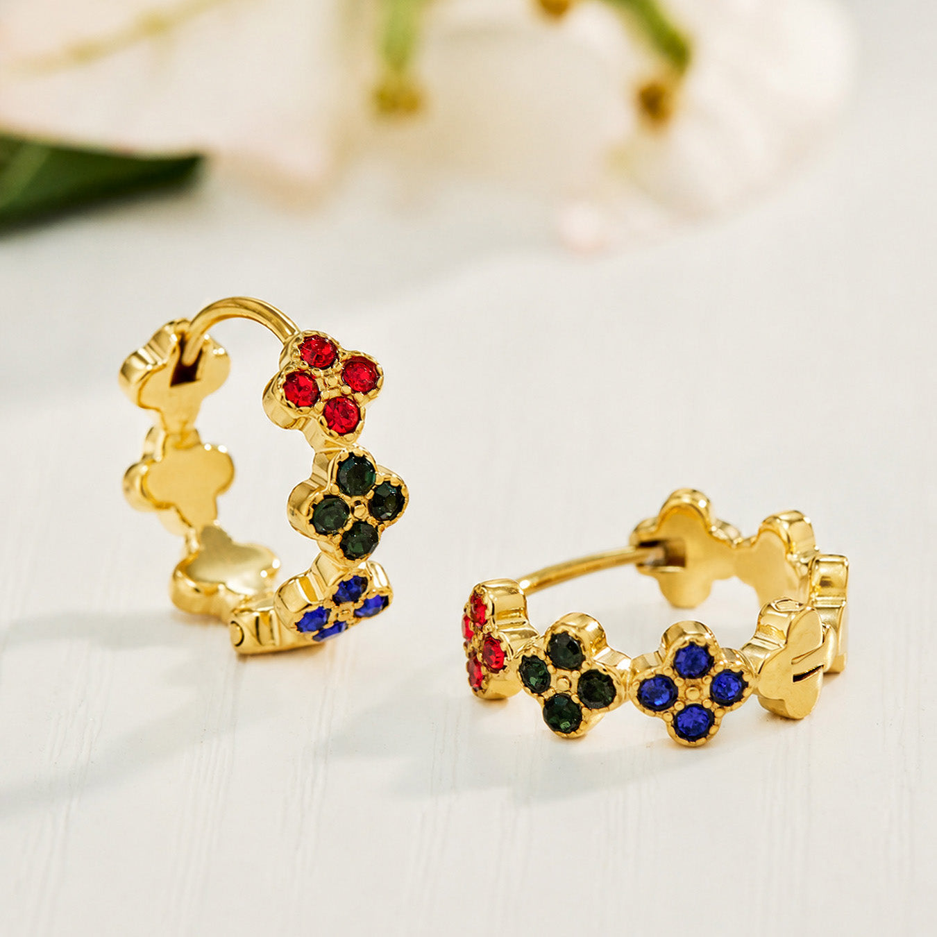 Gold four-leaf clover hoop earrings with multicolor cubic zirconia on a neutral background