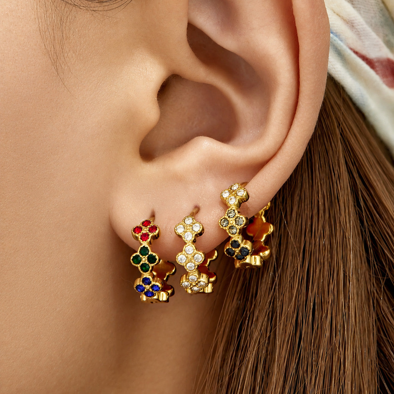 Gold multicolor cubic zirconia clover huggie earrings worn on the ear