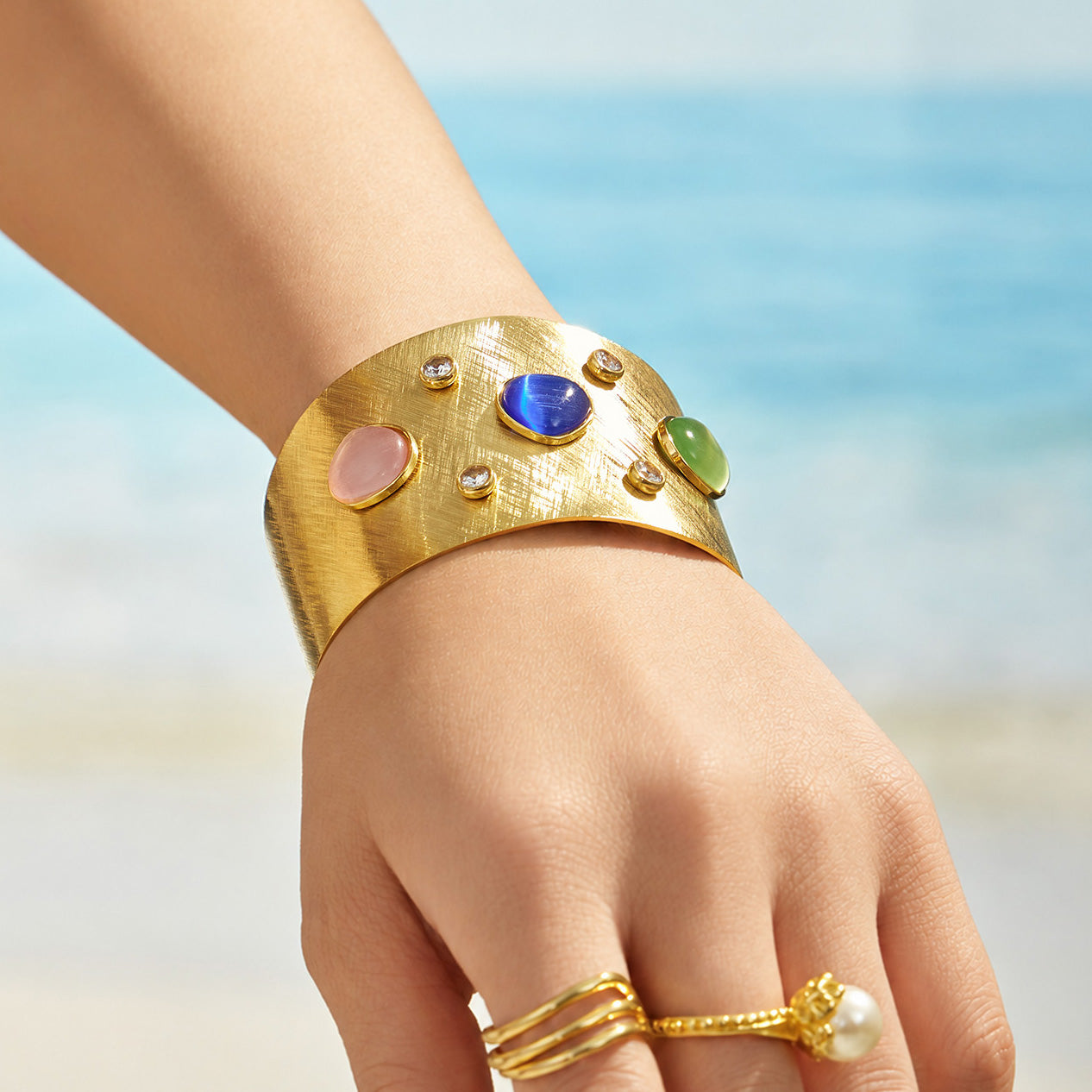 Gold multicolor statement cuff bracelet worn on the wrist at the beach