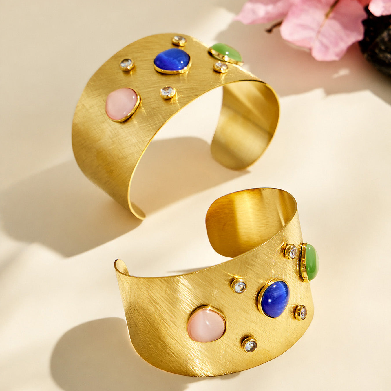 Pair of gold multicolor cuff bracelets displayed on a neutral surface with floral details