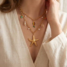 Gold ocean charm necklace featuring starfish, shell and fish motifs worn at the neckline