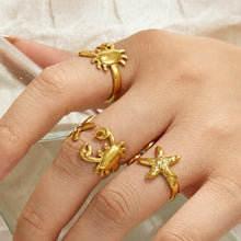Close-up of gold ocean-inspired rings with crab and starfish motifs worn together on a model hand
