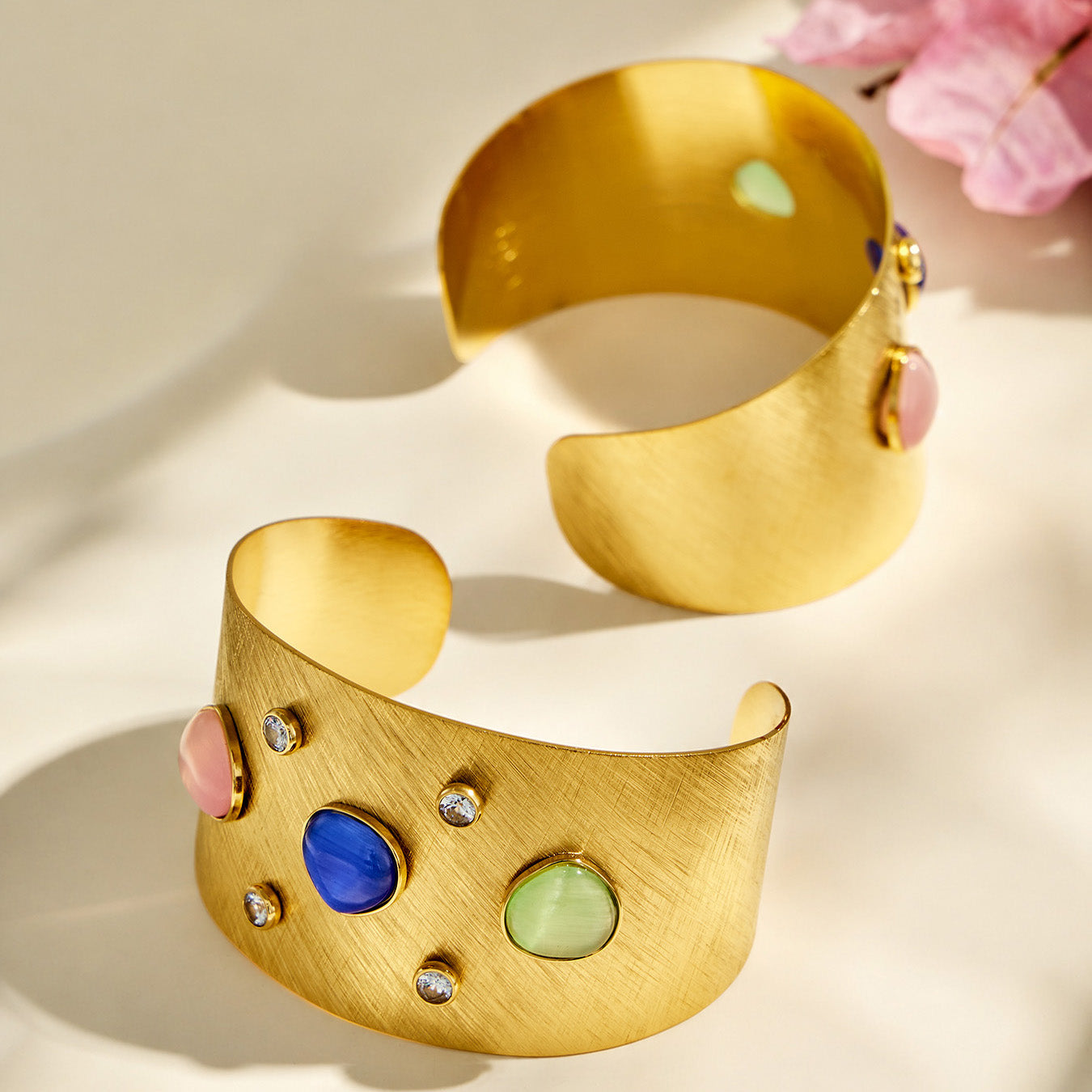 Front and back views of a gold open cuff bracelet with multicolor cat-eye effect stones