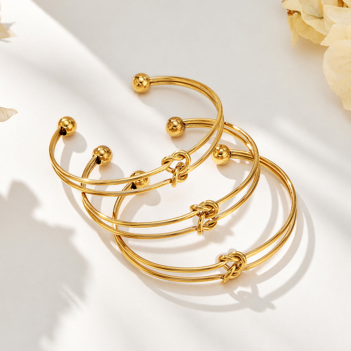 Gold-tone open cuff knot bracelets with polished double wire construction displayed together