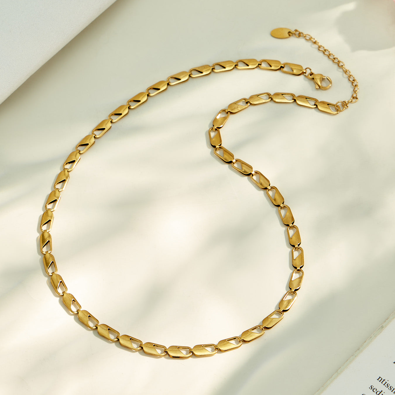 Gold oval link chain necklace arranged in a circular flat lay on neutral fabric