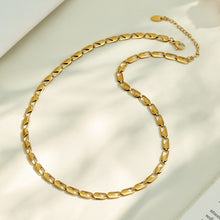 Gold oval link chain necklace arranged in a circular flat lay on neutral fabric