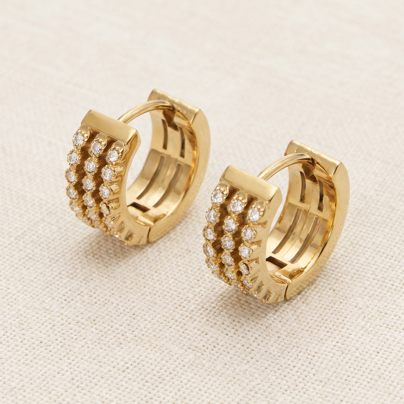 Pair of gold pavé zircon huggie earrings standing on a neutral beige background