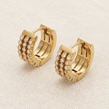 Pair of gold pavé zircon huggie earrings standing on a neutral beige background