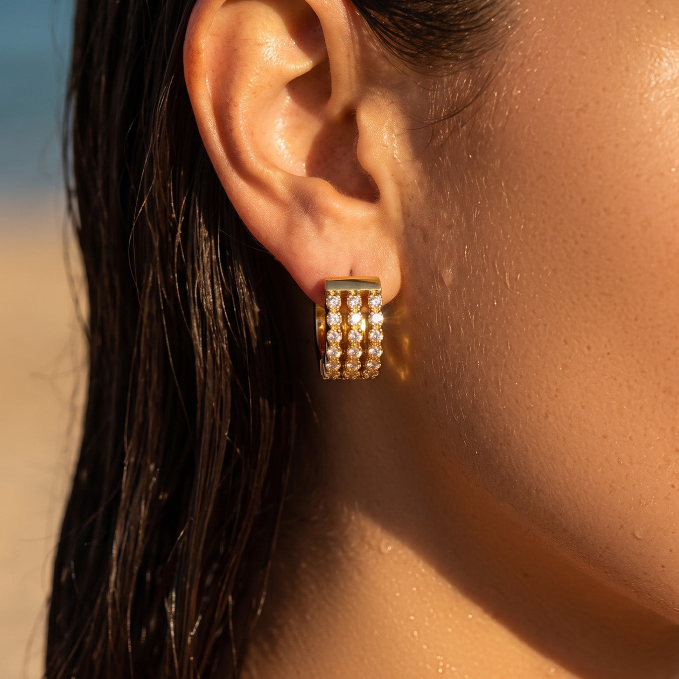 Close-up of small gold pavé zircon huggie earrings worn on the earlobe
