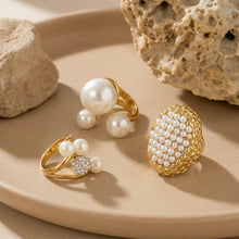 Gold pearl cluster and open-band rings arranged on textured neutral fabric