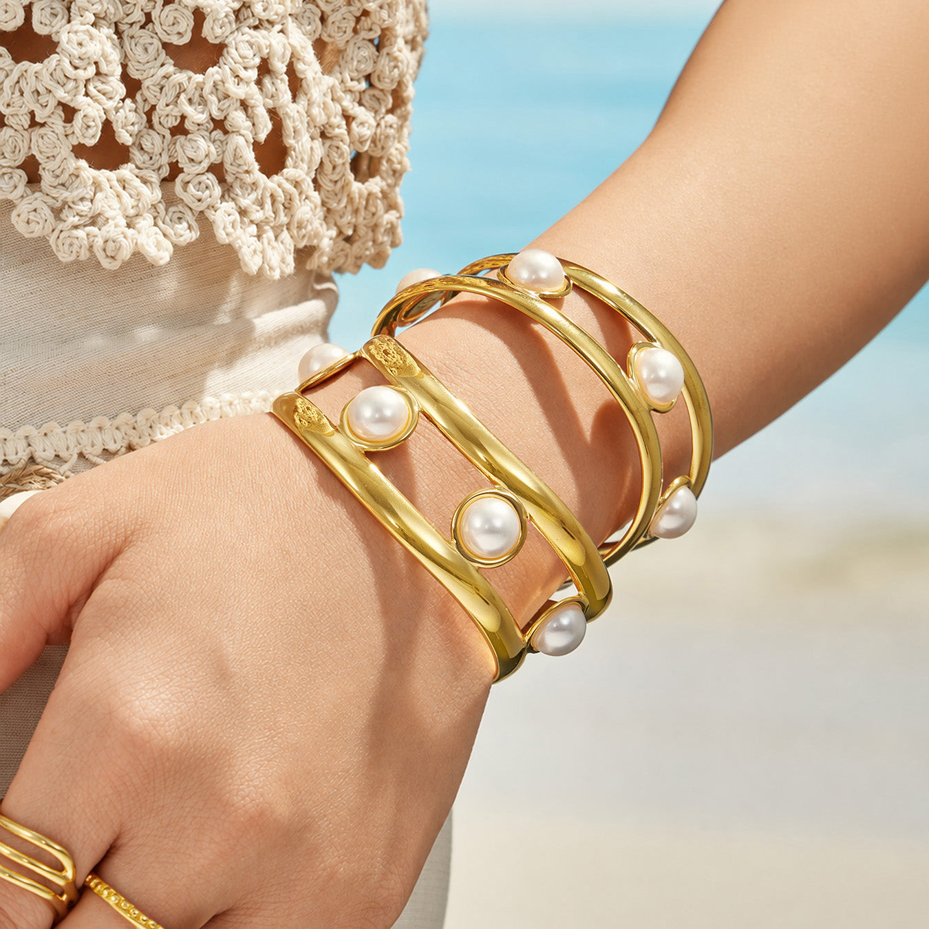 Gold pearl cuff bracelet layered with coordinating bracelets on a model wrist