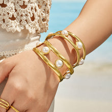 Gold pearl cuff bracelet layered with coordinating bracelets on a model wrist