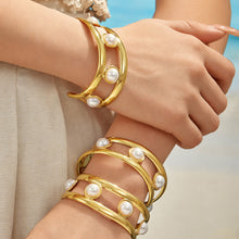 Gold faux pearl cuff bracelet stacked with slim bracelets on a model wrist