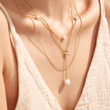 Close-up of a model wearing layered gold necklaces with a white faux pearl drop