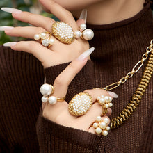 Gold faux pearl rings worn on a hand against a deep green background
