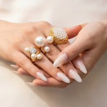 Gold faux pearl statement rings styled across both hands on a light background