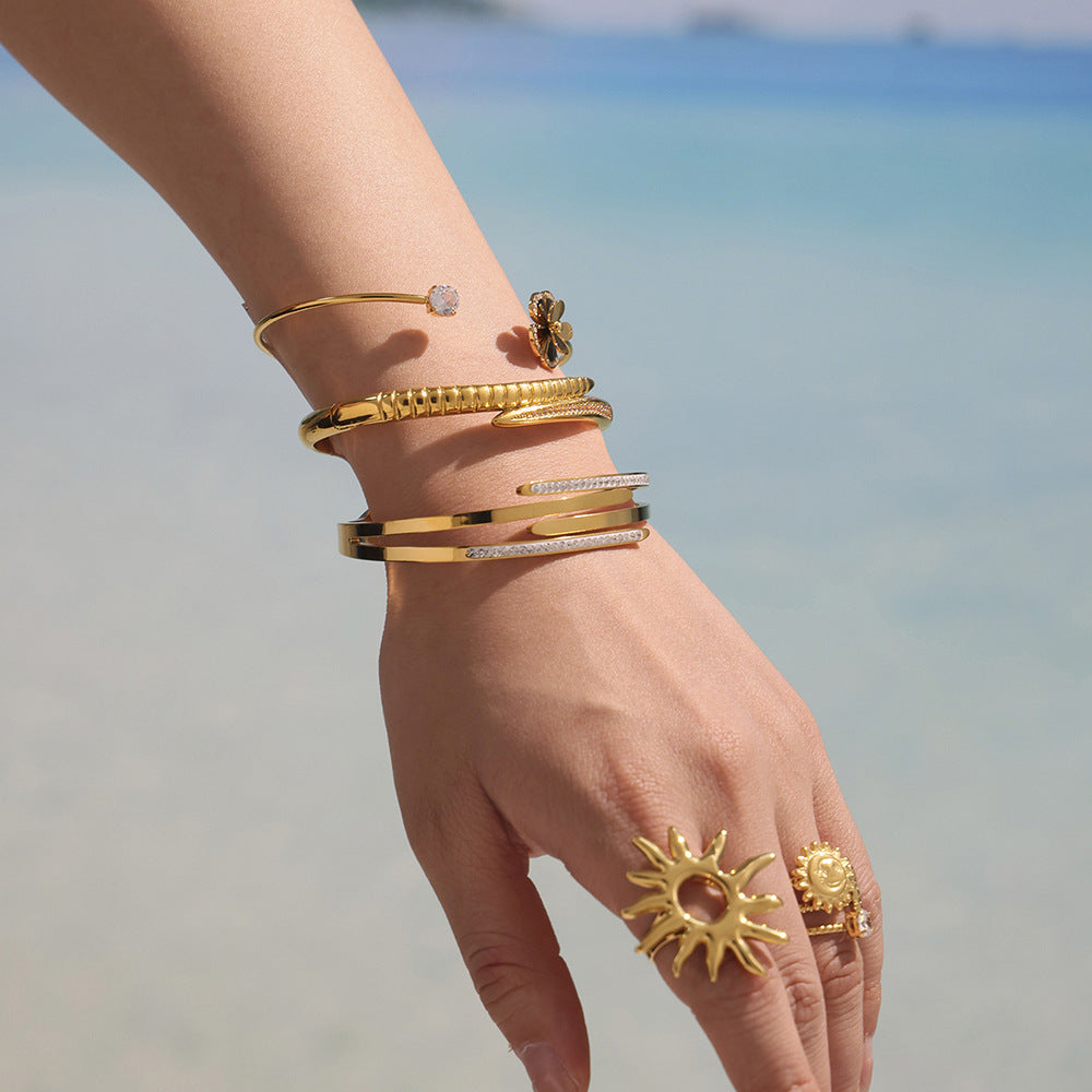 Gold-tone nail bangle bracelet styled with layered bangles and statement rings by the sea