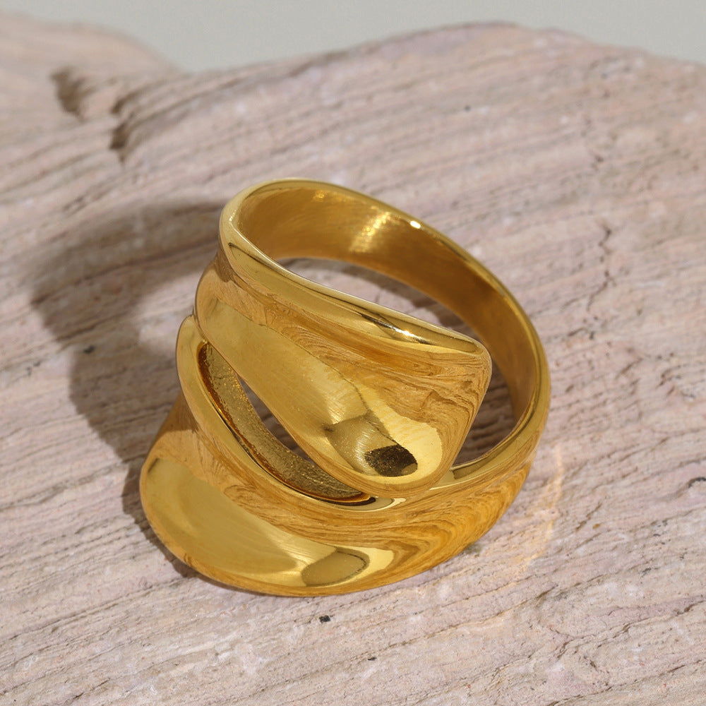 Chunky gold sculptural cutout ring displayed on a textured neutral stone surface
