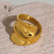 Chunky gold sculptural cutout ring displayed on a textured neutral stone surface