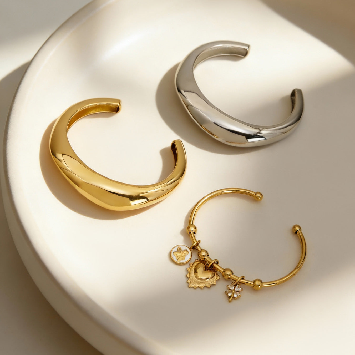 gold silver c-shaped polished stainless steel bracelet set displayed in bowl, modern minimalist jewelry