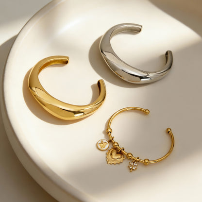 gold silver c-shaped polished stainless steel bracelet set displayed in bowl, modern minimalist jewelry