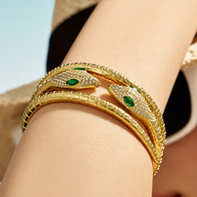 Close-up of stacked gold snake open bangles with green zircon eyes on a model