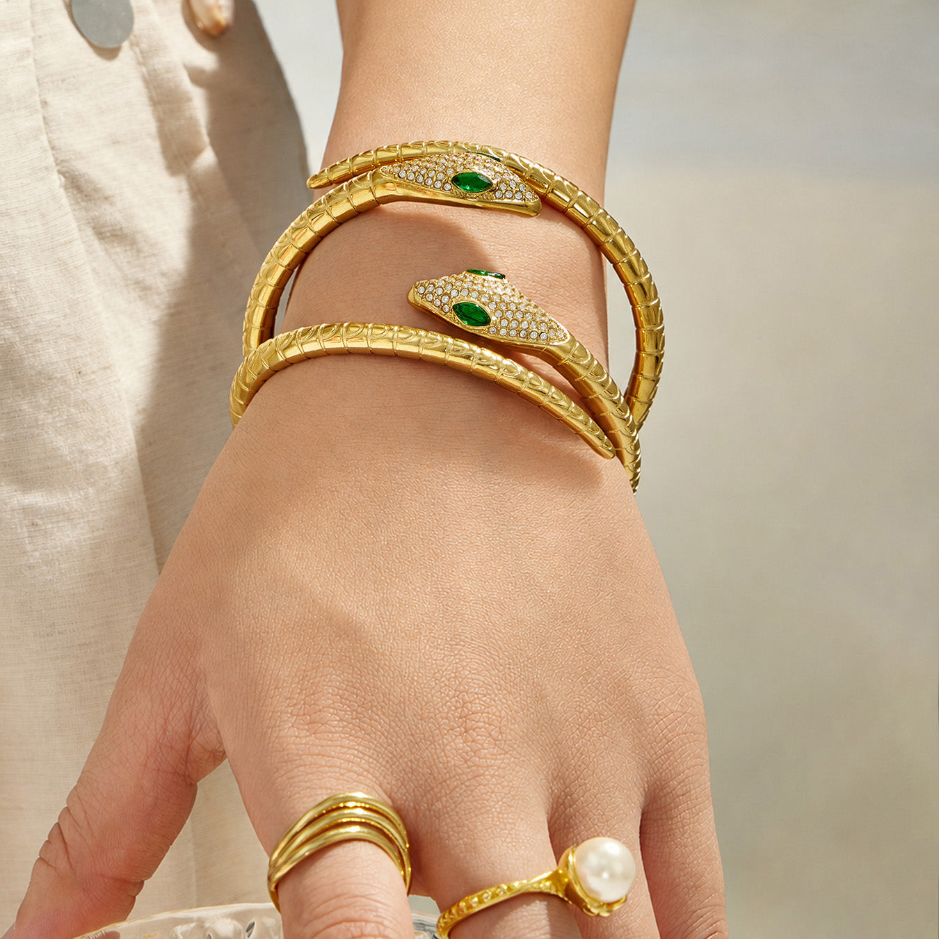 Model wearing stacked gold snake open bangles with matching gold rings