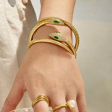 Model wearing stacked gold snake open bangles with matching gold rings