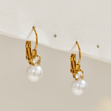 Pair of gold-tone stainless steel pearl drop earrings displayed upright, featuring curved leverback-style hooks and round white pearls