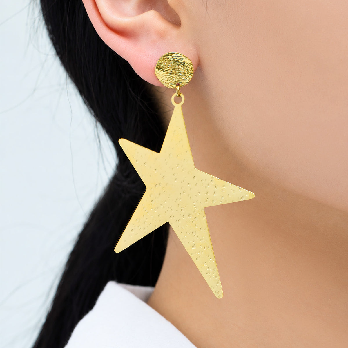 Gold-tone stainless steel star dangle earrings worn on ear for statement styling