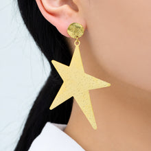 Gold-tone stainless steel star dangle earrings worn on ear for statement styling