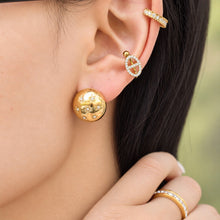 Gold-tone dome earring with clear star-shaped accents worn on a model's earlobe with additional gold ear jewelry