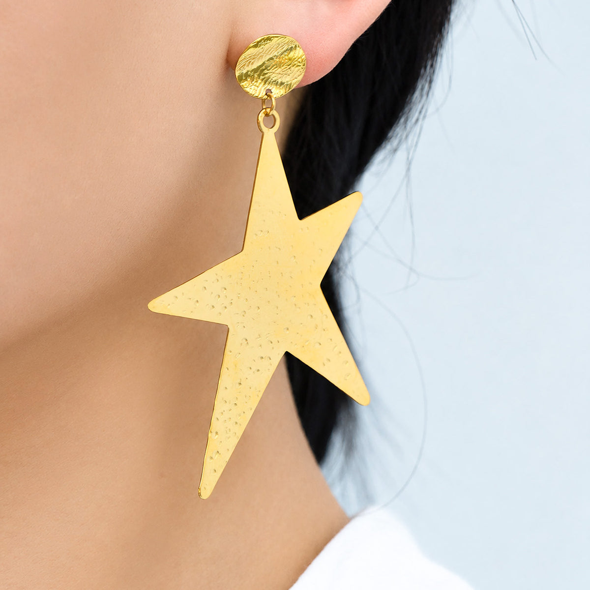 Gold-tone stainless steel star drop earrings worn on ear in side view