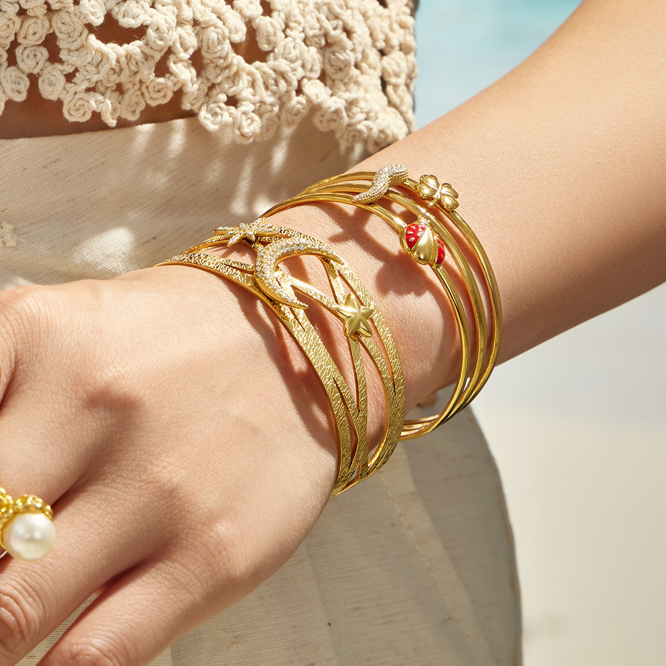 Close-up of layered gold cuff bracelets with celestial and red chili pepper details