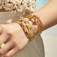 Close-up of layered gold cuff bracelets with celestial and red chili pepper details