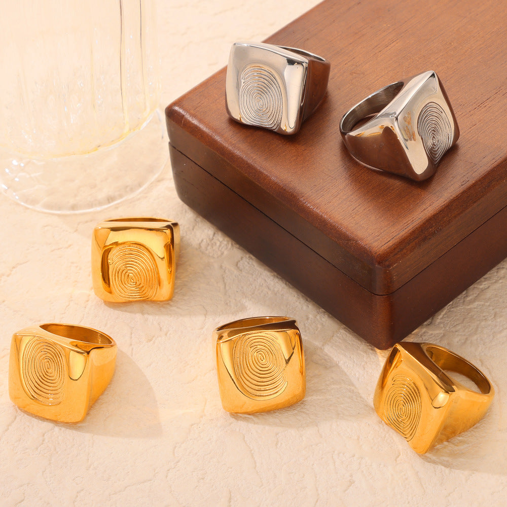 Chunky fingerprint rings in gold and steel finishes displayed with wide sculptural bands