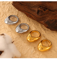 Four organic cutout rings in gold-tone and steel-tone finishes beside a wooden prop
