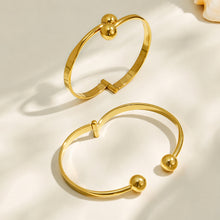Gold and polished steel double ball cuff bracelets arranged together on a neutral background