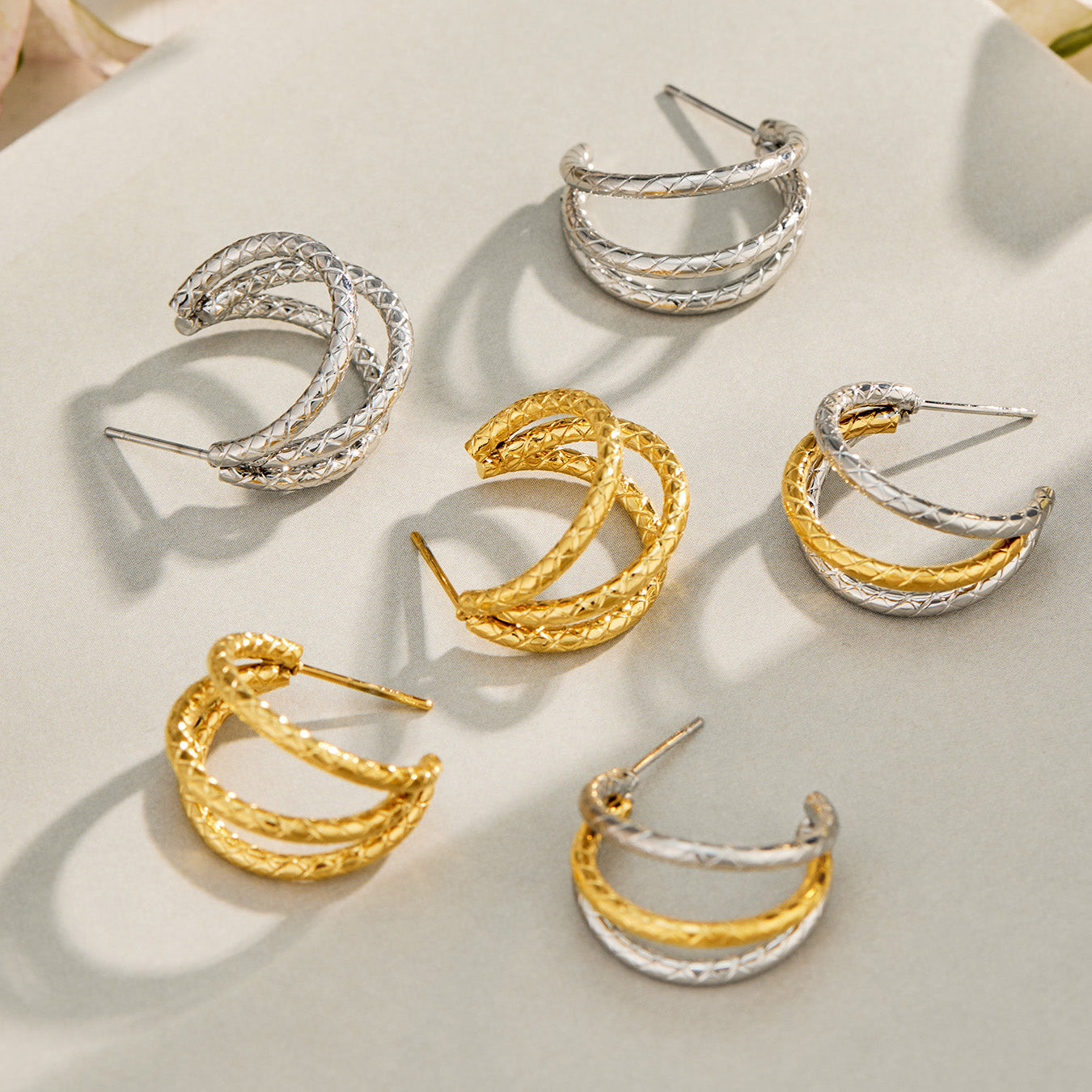 Gold and steel double layer hoop earrings arranged together on a neutral jewelry display