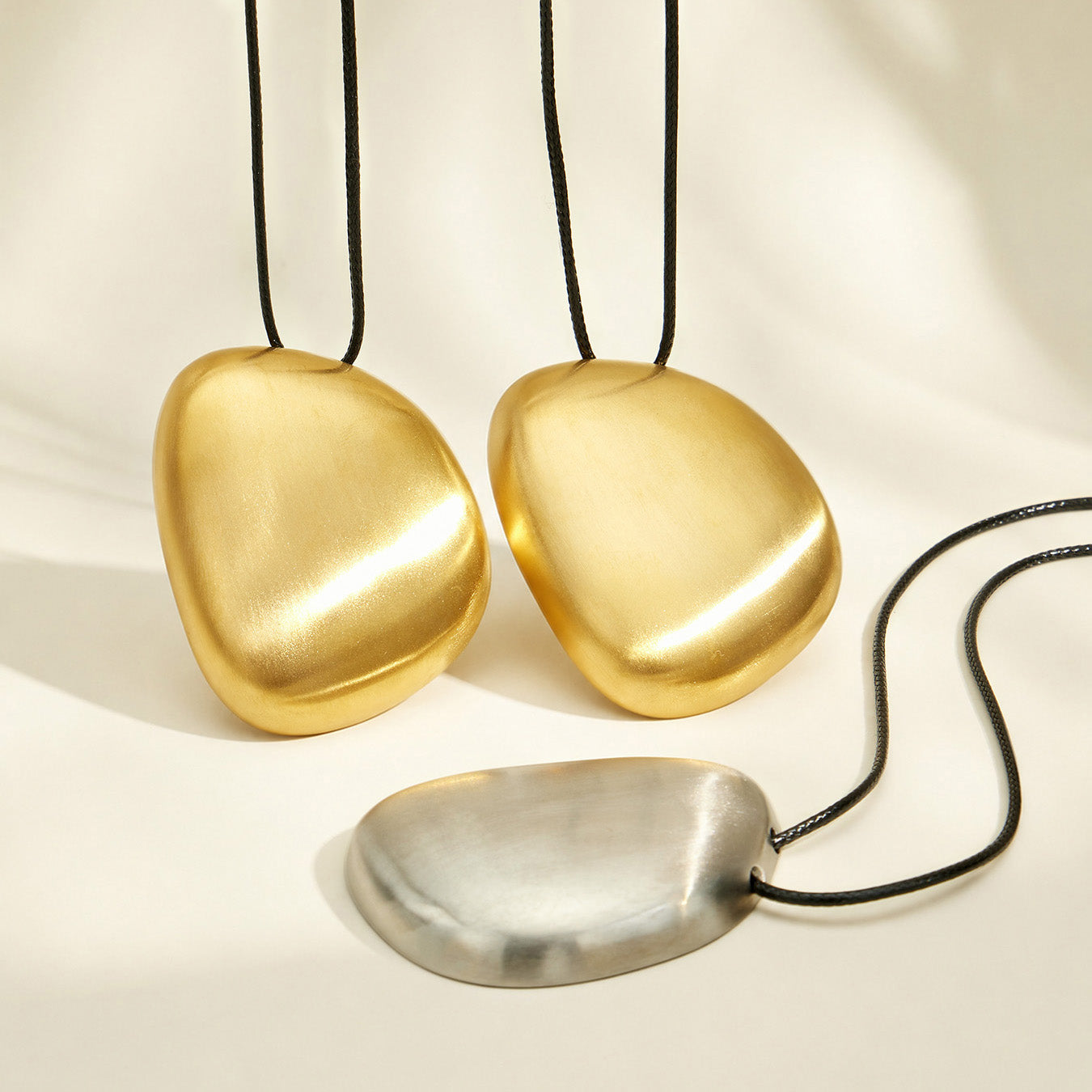 Gold-plated and polished steel pebble pendant necklace finish options displayed together