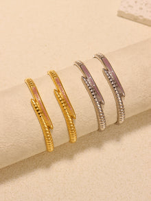 Gold-tone and steel-tone nail bangle bracelets arranged on a cream cylindrical display