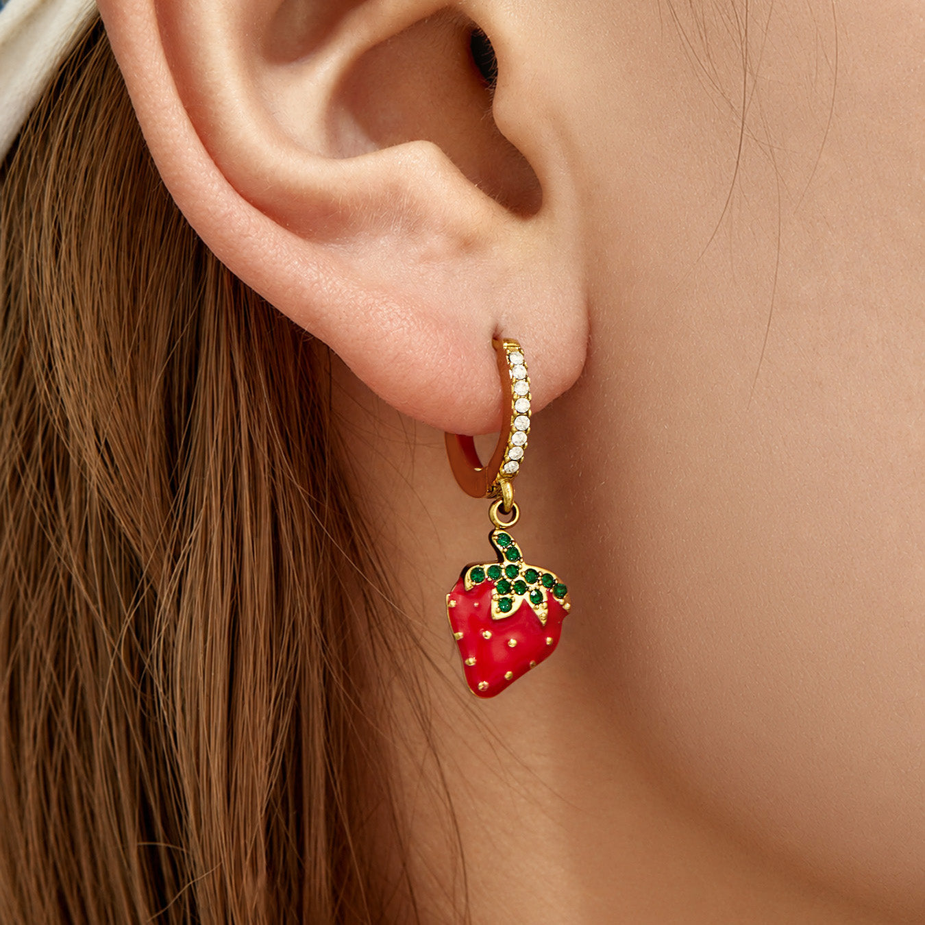 Single gold strawberry charm huggie earring worn on the earlobe