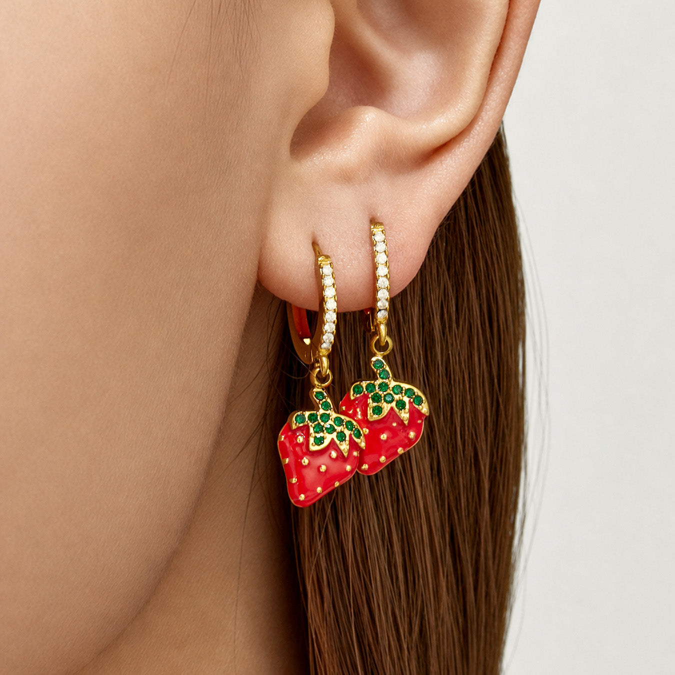 Close-up of gold strawberry charm huggie earrings worn on the ear