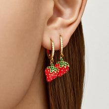 Close-up of gold strawberry charm huggie earrings worn on the ear