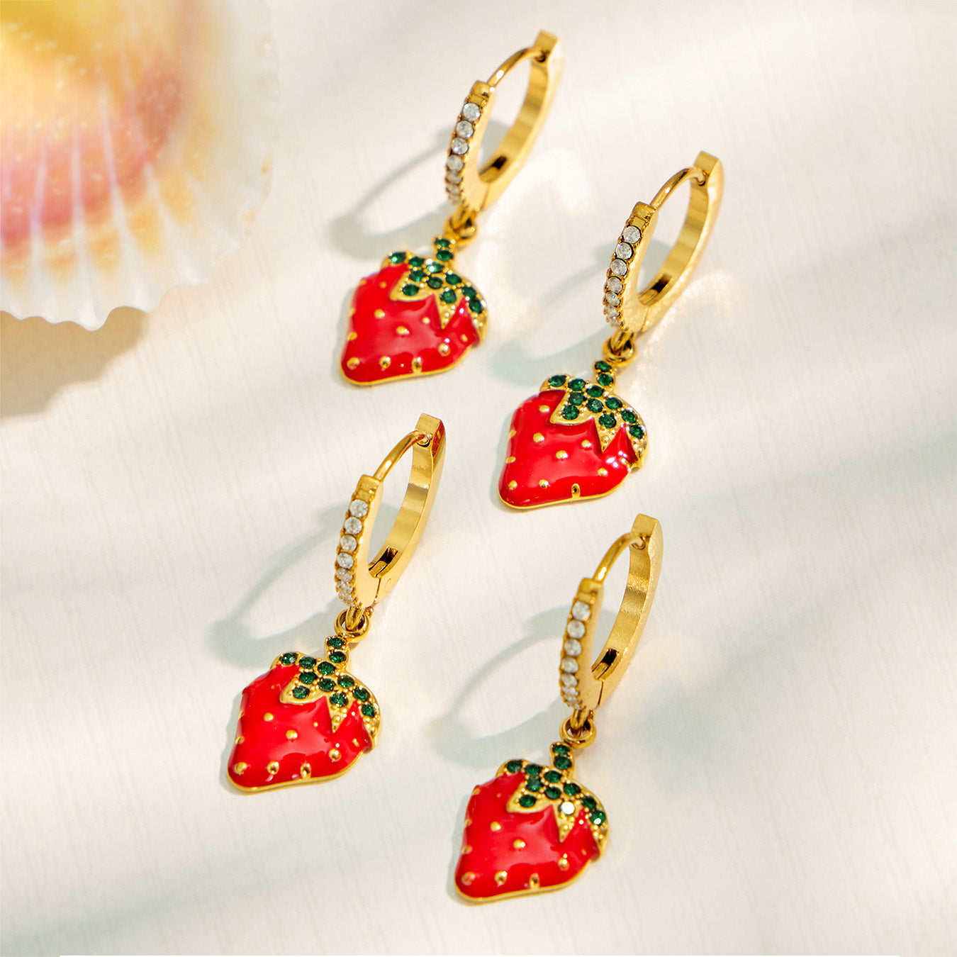 Multiple gold strawberry charm huggie earrings arranged on a light jewelry display
