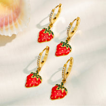 Multiple gold strawberry charm huggie earrings arranged on a light jewelry display