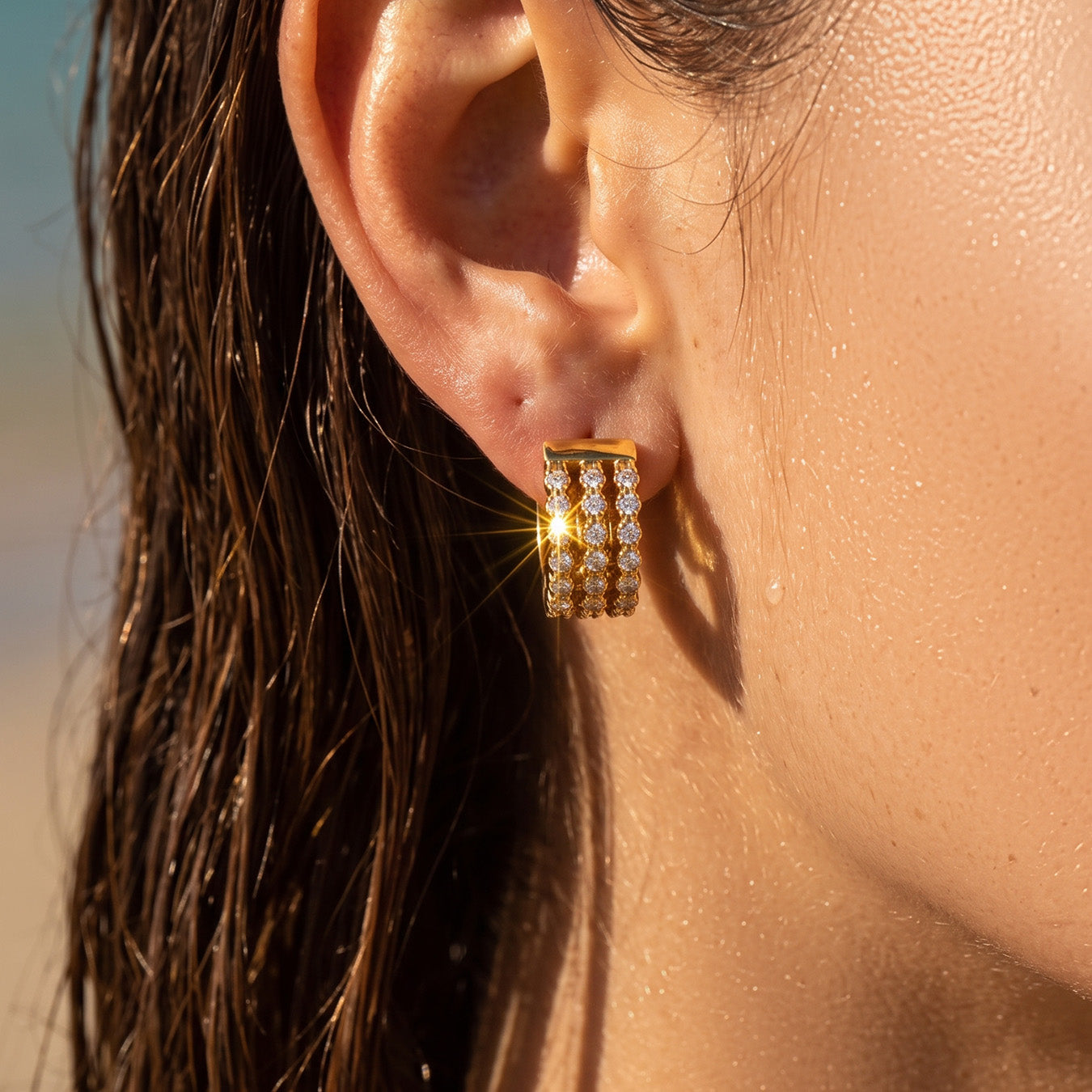 Model with wet dark hair wearing gold triple-row zircon huggie earrings