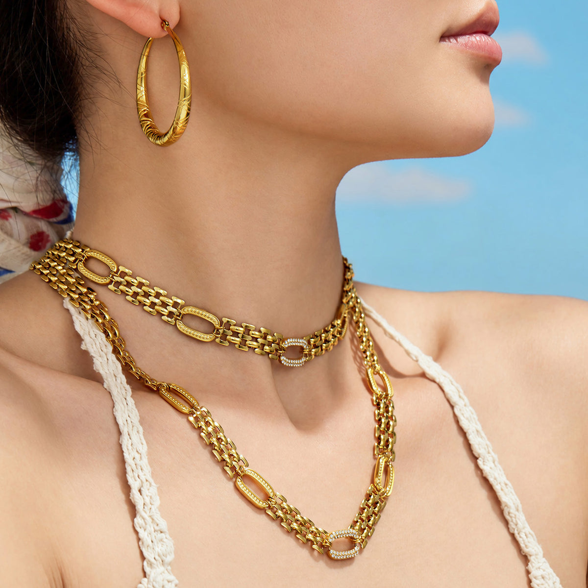 Gold-tone watch band chain necklace layered on model with zircon link details